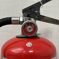 Close-up of the pressure gauge and metal valve on a red fire extinguisher.